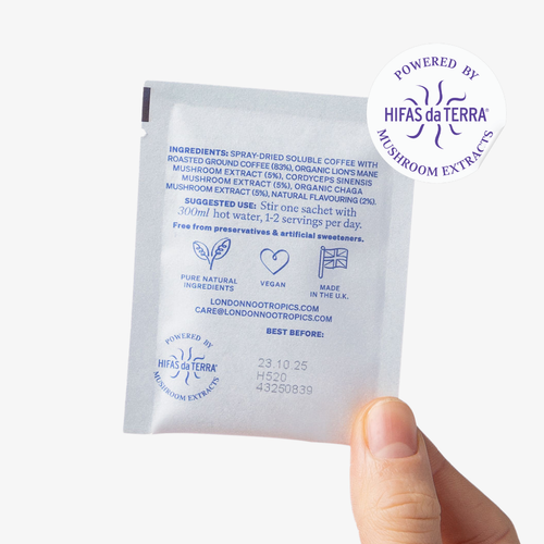 Hand holding a single-serve blue sachet of London Nootropics adaptogenic coffee with Lion's Mane, Cordyceps and Chaga. The blend featured is a Fantastic Fungi collaboration. The image shows a sticker icon at the top right corner of the sachet that reads: Powered by Hifas da Terra Mushroom Extracts.