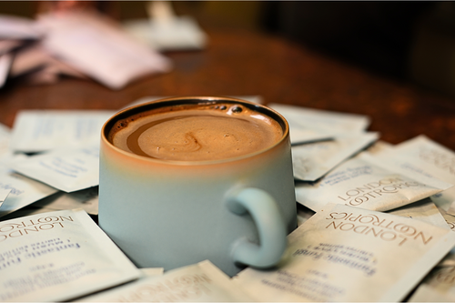 London nootropics adaptogenic coffee in lake blue glaze mug. The mug is surrounded by single serve sachets of Mush Love coffee.