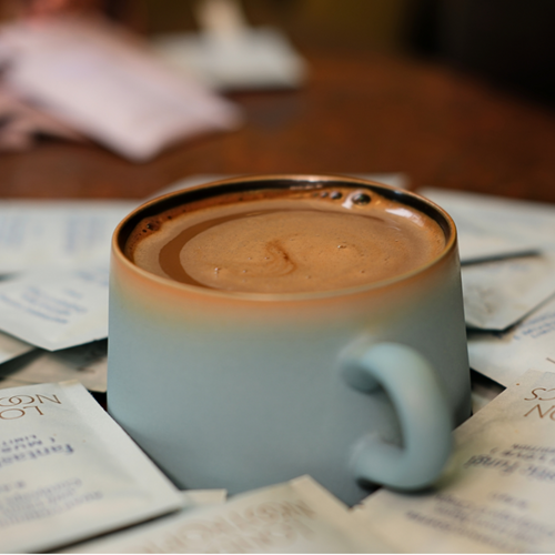 London nootropics adaptogenic coffee in lake blue glaze mug. The mug is surrounded by single serve sachets of Mush Love coffee.