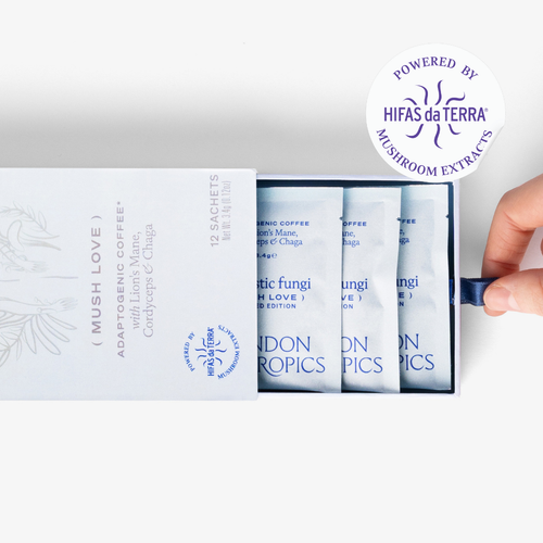 Slightly opened box of Mush Love Lion's Manne, Cordyceps, and Chaga adaptogenic coffee showing three single serve sachets. A hand pull the box open. In the top right corner is a sticker that reads: Powered by Hifas da Terra mushroom extracts.