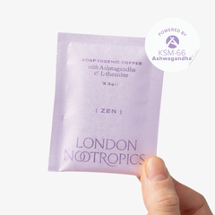 Hand holding a single-serve green sachet of London Nootropics Zen ashwagandha coffee. The image shows a sticker icon at the top right corner of the sachet that reads: Powered by KSM-66 Ashwagandha.