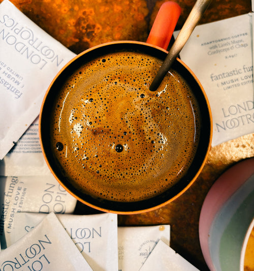 Overhead image of a mug full of London Nootropics adaptogen coffee sitting atop a surface covered in Mush Love coffee sachets.