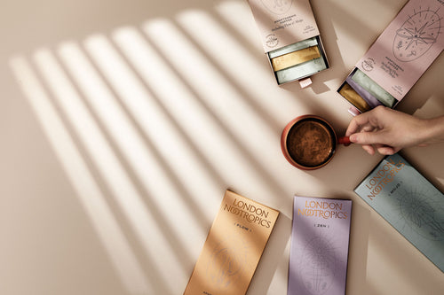 Overhead image of a mug of London Nootropics coffee surrounded by various colours of London Nootropics coffee boxes.